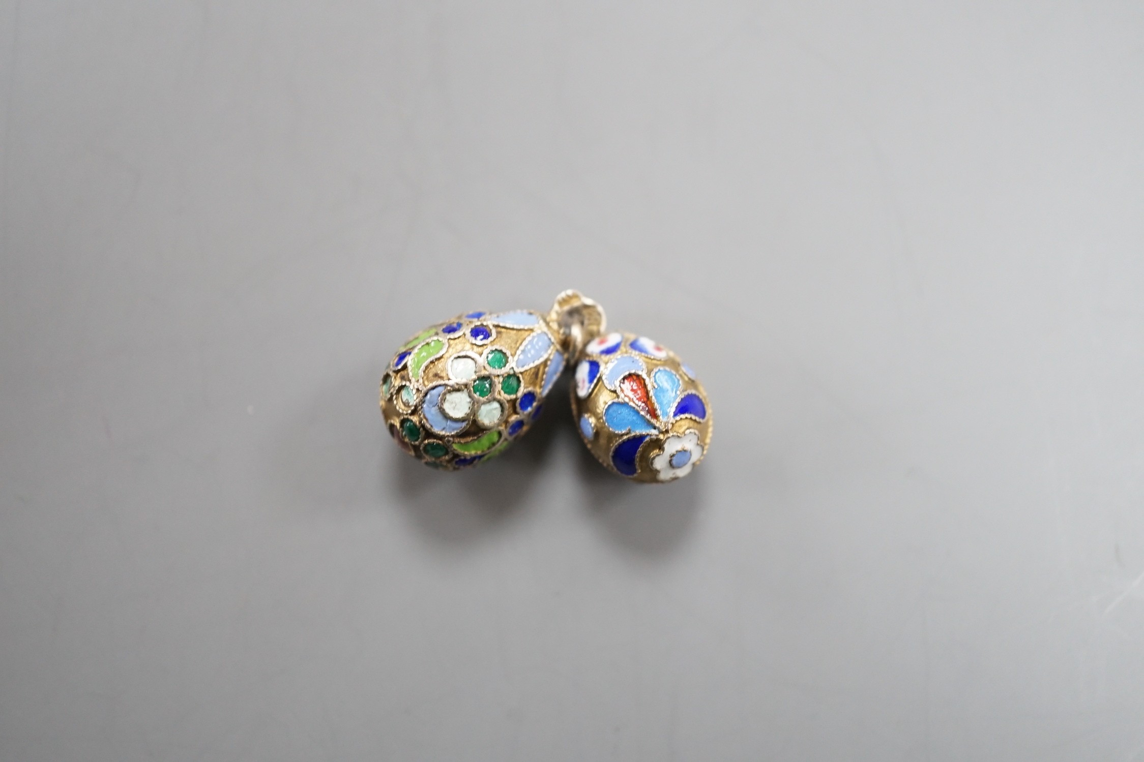 An early 20th century Russian 84 zolotnik and polychrome cloisonné enamel set egg pendant, maker's mark HT?, 17mm and a similar smaller egg pendant, maker's mark HM?.